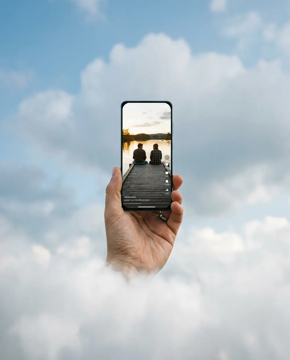A hand holds an iPhone up out of the clouds. At 4:21 it shows a short-video feed: two friends on a jetty at golden hour, with likes and comments.
